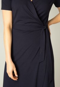 Marineblaue Wickelkleid aus weichem Stoff, mit tiefem V-Ausschnitt, kurzen Ärmeln und einem Taillengurt für eine verstellbare Passform.