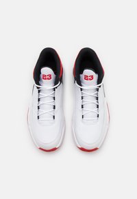 Białe skórzane buty sportowe z czarnymi i czerwonymi akcentami, z sznurowanym zapięciem i wyprofilowanym językiem dla komfortu. Teksturowana podeszwa środkowa i zewnętrzna.
