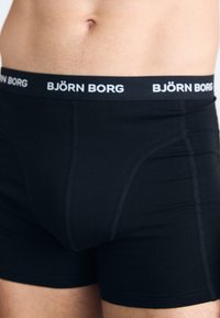 Schwarze Boxer-Briefs aus Stretchgewebe, mit einem breiten schwarzen Bund, der das weiße Logo "BJÖRN BORG" und kontrastierende Nähte aufweist.