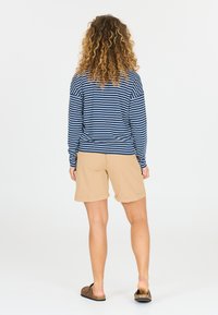 Randig marinblå långärmad topp med krämfärgade ränder, tillsammans med beige shorts. Shortsen har upprullade fållar och är gjorda av ett lätt tyg.