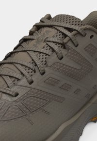 Κοντινό πλάνο καφέ παπουτσιού τρεξίματος Hoka με πλέγμα στο πάνω μέρος και λεπτομερή κορδόνια.