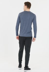 Långärmad, melerad blå träningsskjorta parat med svarta, figurnära byxor. Klädseln har en mjuk textur och en avslappnad design.