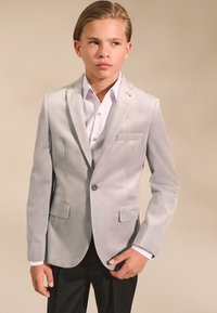 Hellgrauer Blazer aus weichem Stoff mit Reverskragen, zwei Vorderentaschen und einem Knopfverschluss, kombiniert mit einem weißen Hemd.