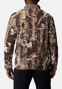 Tarnfleecejacke in erdigen Tönen mit einem Waldmuster, hohem Kragen und weicher Textur. Ideal für Aktivitäten im Freien.