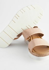 Tan faux leather sandals with two wide straps, a cushioned footbed, and a white rubber sole featuring textured grip patterns and metallic accents.