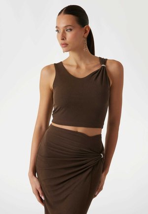 Braunes Cropped-Top mit einem drapierten Schulterdesign und silbernem Akzent, kombiniert mit einem passenden hochgeschnittenen Rock mit geraffter Textur.