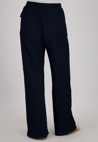 Navyblauwe broek van textuurstof, met een trekkoord in de taille en een wijde pijpdesign. Geen zichtbare merknamen of accenten.