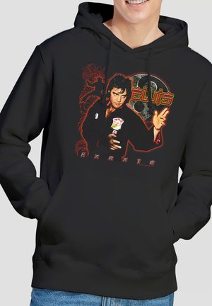 Mann trägt schwarzen Hoodie mit farbenfrohem Grafikmotiv von Elvis Presley in Karate-Pose, rotem Drachen und dem Wort "Karate" in stilisierter Schrift.