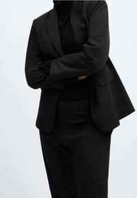 Costume noir sur mesure avec un blazer structuré et un pantalon assorti. Texture lisse, sans motifs visibles, et un design classique et professionnel.