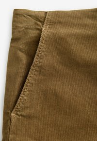 Khaki kordurovátová tkanina s vertikálními žebry, s detaily švu kapsy a kontrastním stehem na okraji. Viditelná měkká textura.