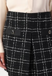 Black and white checkered skirt with a textured weave, featuring two side pockets with black fabric accents and circular hardware details.