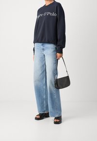 Granatowy sweter z białym napisem, jasnoniebieskie spodnie szerokie w nogawkach, czarna torebka o fakturze, oraz czarne platformy z grubą podeszwą.