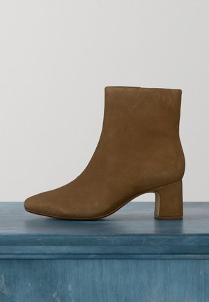 Brauner Wildleder-Stiefelette mit Blockabsatz, abgerundeter Spitze und glatter Textur auf einer blauen Holzoberfläche.
