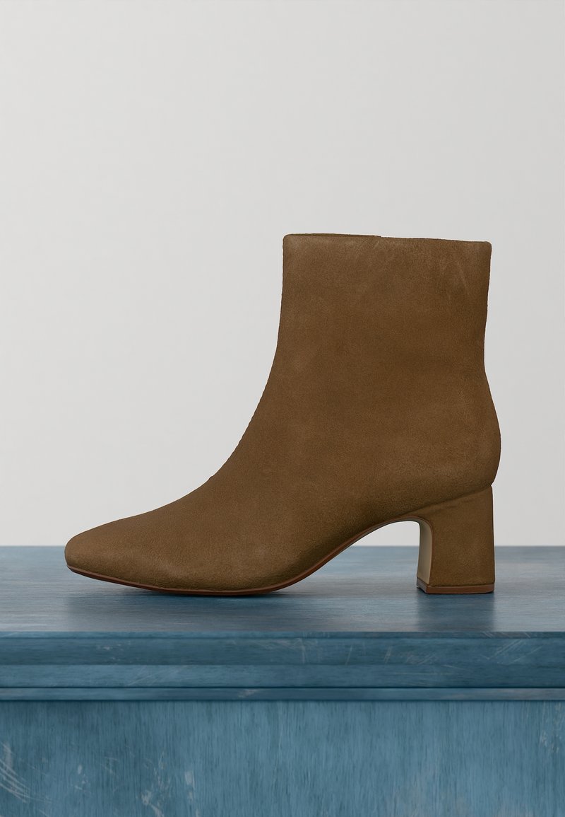 Bottine en daim marron avec talon bloc, bout arrondi et texture lisse posée sur une surface en bois bleu.