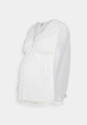 Witte zwangerschapsblouse met lange doorschijnende polkadotmouwen, V-hals, knoopsluiting aan de voorkant en een geplooid detail in de taille.