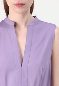 Hihaton violetti pusero V-pääntiellä, jossa on hienovaraiset ompeludetaljit ja sileä, kevyt kangas.