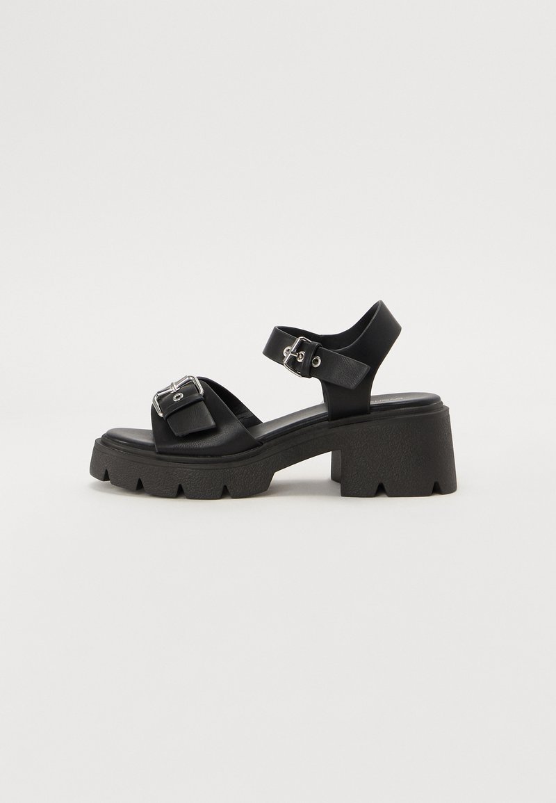 Black platform sandals made of textured material with a chunky heel and adjustable straps. Features a buckle detail on the upper strap.