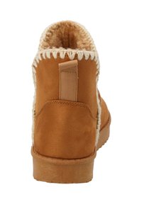 Bottine en suède marron avec une doublure en polaire crème douce et descoutures décoratives crème le long du col. Dotée d'une languette.