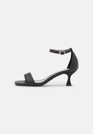 Sandale pour femmes noire texturée à bout ouvert avec fine bride à la cheville et talon bas courbé sur fond blanc.