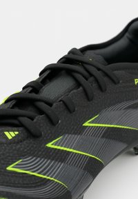 Black soccer cleat with textured upper, featuring neon green accents and lines, and black laces. Close-up on the forefoot area.