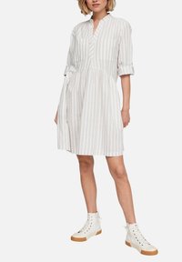 Robe rayée, jusqu'au genou, en tissu léger avec un décolleté en V et deux poches poitrine. Accompagnée de baskets montantes blanches avec des semelles en cuir. 