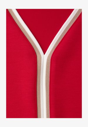 Gros plan sur un tissu rouge avec un bord en forme de V présentant des rayures blanches et beige le long des bords.