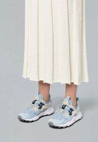 Zapatillas deportivas con un upper texturizado en azul claro y crema, detalles en azul marino y una suela de goma gris. Presenta un cuello acolchado y cordones.