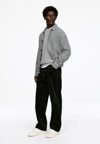 Black and white checkered jacket over a gray sweater, paired with dark green corduroy pants and white sneakers. Smooth fabrics and relaxed fit.