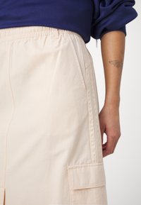 Heledbeez värvi seelik elastse vöökohtadega, külje taskuga ja peene ruudulisusega tekstuuriga. Omab külgedel tikkimiseks õmmeldud õmblusi detailideks.