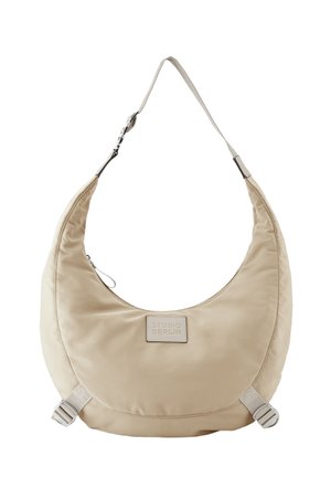 Beige, halbmondförmige Schultertasche mit verstellbarem Riemen, Reißverschluss und einem kleinen rechteckigen Aufnäher mit der Aufschrift Studio Berlin.