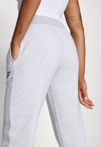 Pantalones de chándal grises de textura suave, con una cintura acanalada, bolsillos laterales y un logotipo sutil en el muslo izquierdo.