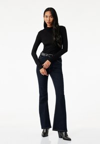 Zwart langslievend shirt met een aansluitend design, gecombineerd met donkerblauwe flared jeans met zichtbare stiksels en een zwarte riem, aangevuld met haklaarzen.