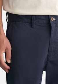 Mørkeblå, letvægts bomuldsbukser med flad front, lynlås, knaplukning og sidelommer, der har en glat tekstur og en skræddersyet pasform.