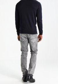 Námořnický svetr s kulatým výstřihem, doplněný světlými šedými džíny s vybledlým vzhledem a zadními kapsami; černé kotníkové boty tvoří dokonalý outfit.