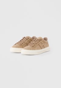 Ζευγάρι μπεζ σουέντ αθλητικά παπούτσια με κορδόνια που ταιριάζουν και λευκές λαστιχένιες σόλες σε ανοιχτό γκρι φόντο.