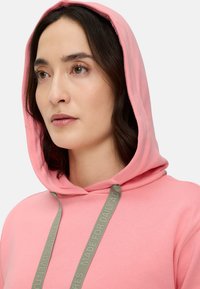 Light pink hoodie with a drawstring featuring gray text. Soft fabric texture, attached hood, and a simple, relaxed design.