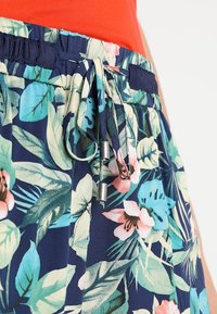 Spodnie w kolorze niebieskim z nadrukiem tropikalnych kwiatów i liści w odcieniach różu, bieli i turkusu, posiadające ściągacz w talii z metalowymi końcówkami.