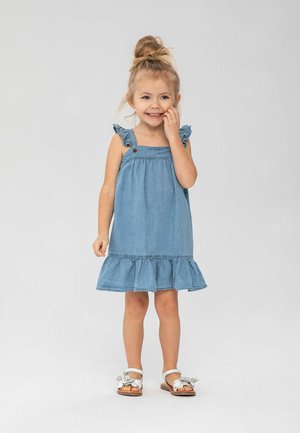 Robe en denim avec des bretelles à volants, une jupe évasée avec un ourlet à volants et un petit bouton rouge en accent. Sandales avec des embellissements floraux.