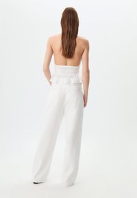 Top bianco senza spalline con ruches sul fondo, abbinato a pantaloni bianchi a gamba larga e vita alta. Tessuto morbido, design minimalista.