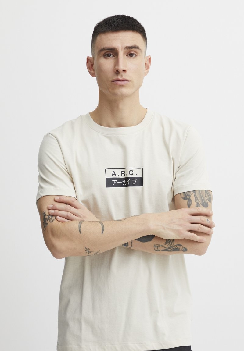 Kremna kratka majica s kratkimi rokavi z črnim pravokotnim grafičnim napisom "A.R.C." in japonskimi znaki. Iz bombažnega materiala, slim fit, krožni izrez.