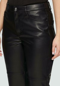 Zwarte leren broek met een slim fit, voorzien van voorkruiszakken, een knoopsluiting en zichtbare naden langs de benen.
