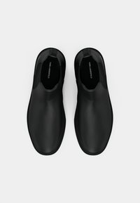 Sapatos slip-on pretos com uma superfície lisa e mate. Forma de bico arredondado, painéis laterais elásticos e design minimalista. Logótipo impresso por dentro.