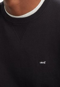 Pull noir avec un col rond côtelé et un petit logo blanc Levi's sur la poitrine gauche. Le tissu semble doux avec une texture lisse.