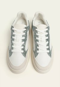 Sneakers bianchi con accenti di glitter argento sui lati, punta rotonda, lacci piatti e una suola beige testurizzata.