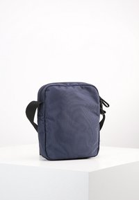 Borsa rettangolare blu navy in tessuto testurizzato, dotata di una zip superiore e di una tracolla per il trasporto. Design semplice e minimal.
