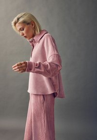 Rosa geripptes Oberteil mit Kragen und Knopfdetails, kombiniert mit passenden weit geschnittenen Hosen. Lässiges und strukturiertes Design.