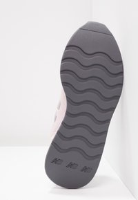 Semelle d'une basket New Balance rose clair avec motif ondulé et trois logos "NB" en relief sur une semelle en caoutchouc grise.