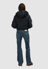 Czarna kurtka puchowa z kapturem, z pikowanym wzorem. Połączona z niebieskimi dżinsami z ozdobnymi kieszeniami i brązowym obuwiem.