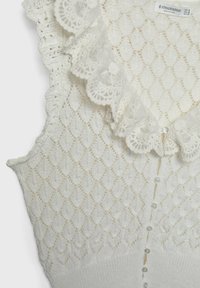 Stickad vit topp med diamantmönster, spetsvolang vid halsen och pärlknappar fram. Mjuk textur med detaljerade accenter.