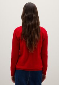 Maglione rosso a maglia con scollo rotondo e maniche lunghe, caratterizzato da una texture liscia e un orlo aderente. La vista posteriore mostra capelli lunghi e fluenti.